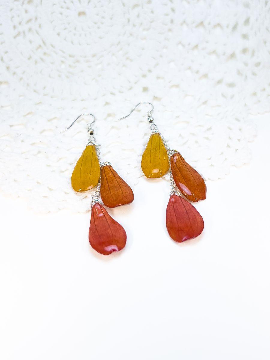 A pair of chandelier earrings made with 3 zinnia petals each, yellow, orange, and red.