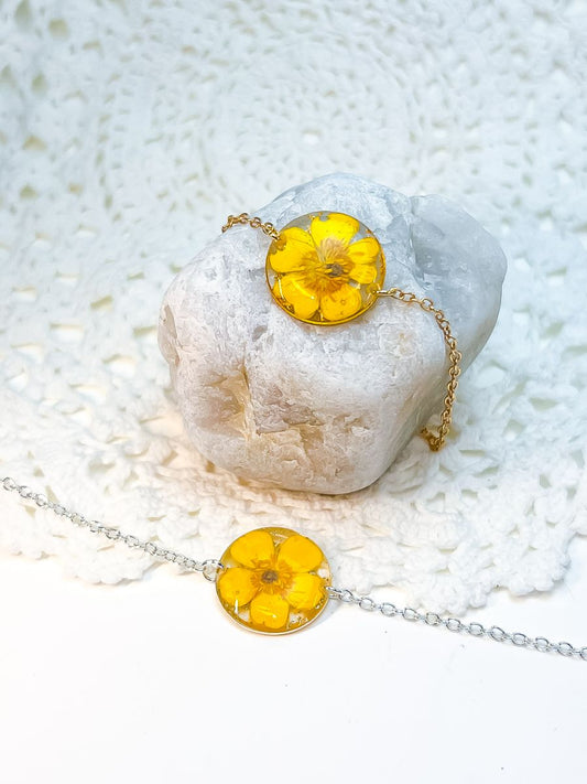 Two round pendant bracelets made with pressed buttercup flowers. Shown in both gold and silver metal.