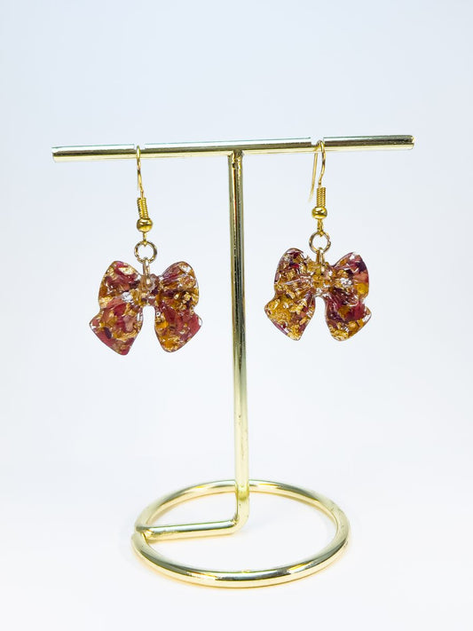 Bow earrings made with crushed maple leaves hanging on a stand.