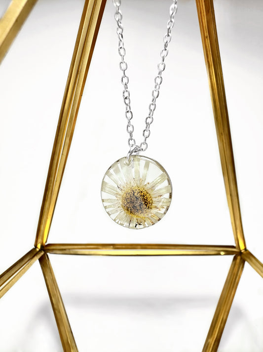 Large silver pressed daisy pendant necklace hanging on display.