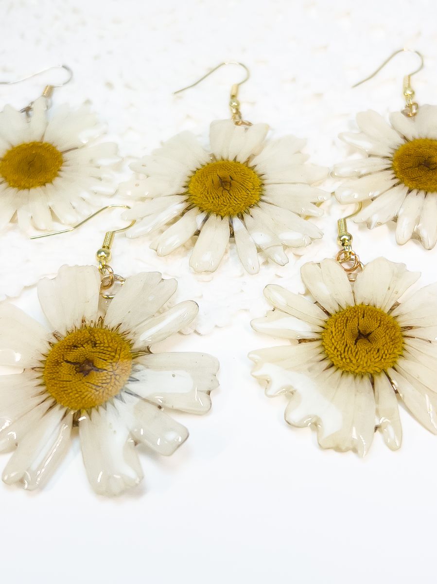 3 pairs of 3D daisy dangle earrings laying on a white surface.
