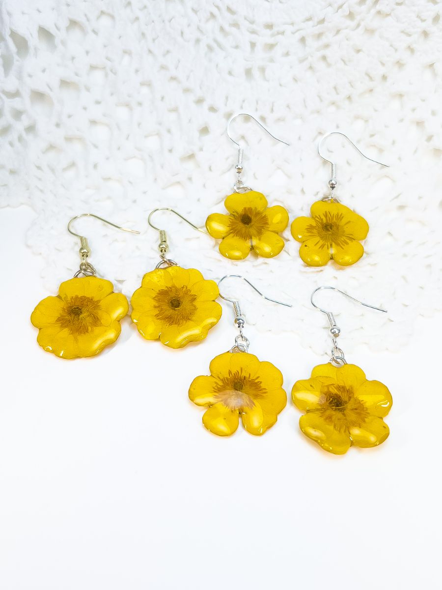 Three pairs of 3D buttercup dangle earrings laying on a white surface.