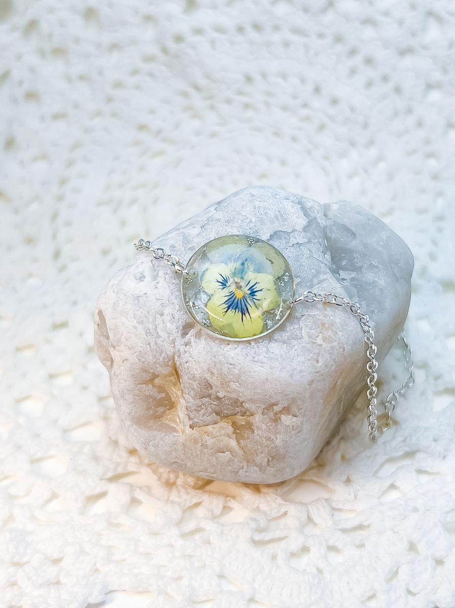 A bracelet made from a real blue violet, clasped around a white rock for display purposes.
