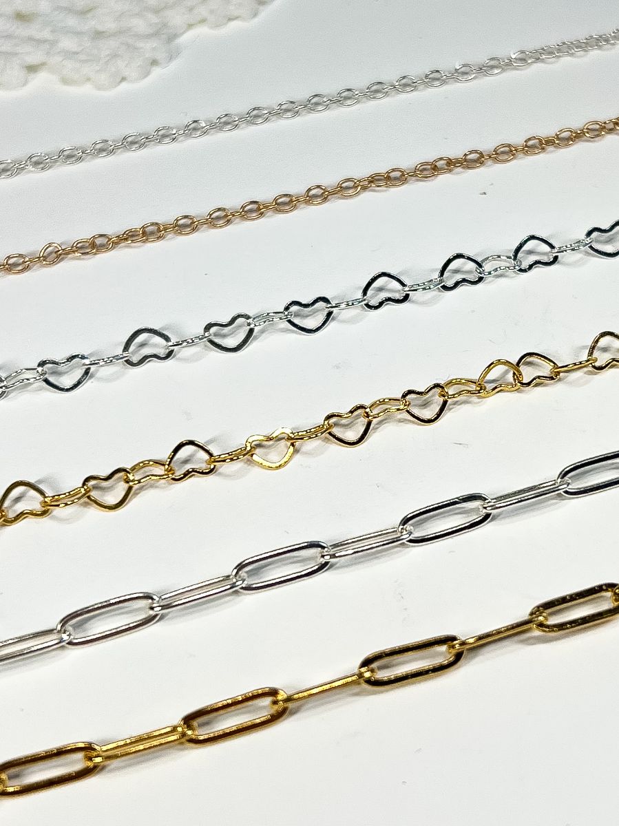 plain chain, heart chain, & paperclip chain laid out in gold and silver.