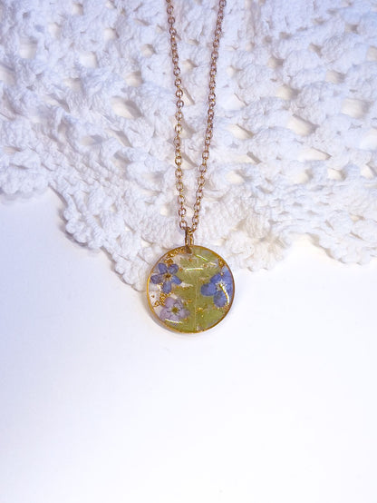 Round pendant necklace made from pressed forget-me-nots and ferns.