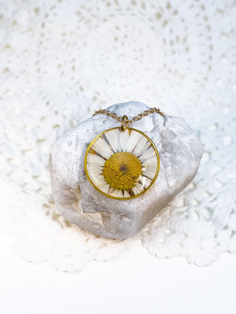 Large pressed daisy pendant necklace displayed on a white rock.