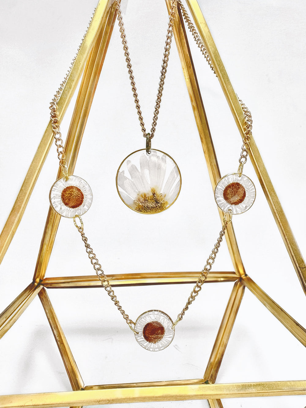 Large daisy necklace stacked with a 3-piece daisy necklace in gold. 